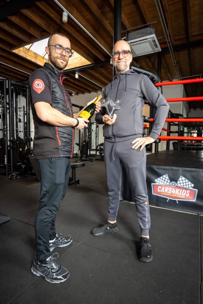 Twee mannen in sportkleding met een fles champagne en glazen bij een bokring in sportschool.