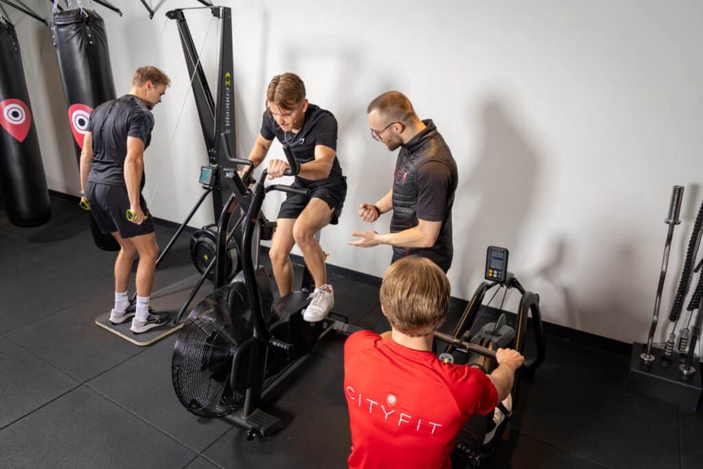 Vier mannen trainen met roeimachine, airbike, springtouwen en coach in sportschool.